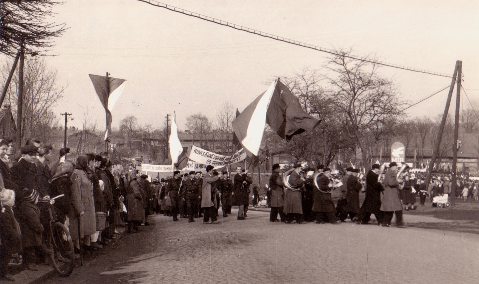 Záběr z manifestace proti zbrojení a nukleárním zbraním v Karviné 14.4.1958. V pozadí vpravo: budova čp. 266 (původně hospodářská budova statku hraběte Larisch-Mönnicha). V pozadí uprostřed: budova čp. 1023. V pozadí vlevo je ještě částečně patrná budova čp. 67 (Kovárna a zámečnictví Max Herz).