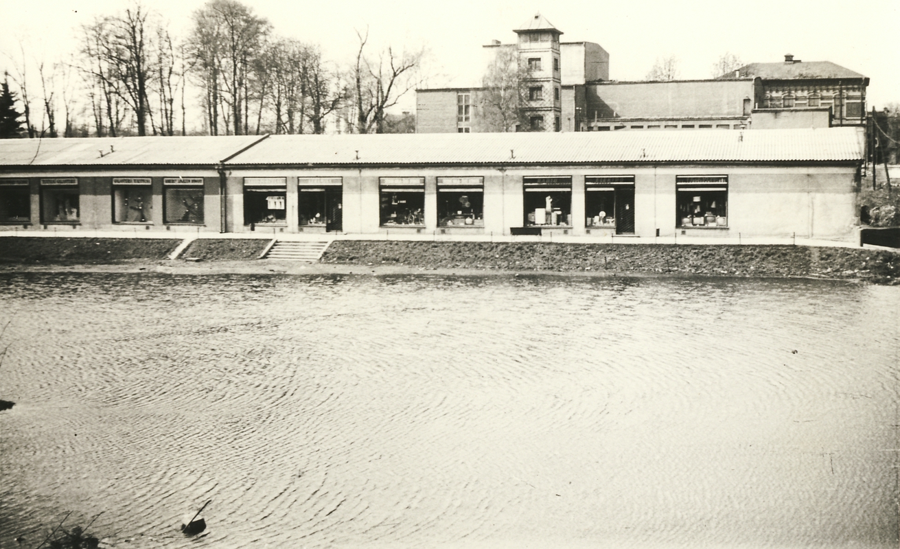 Řada obchodů pod Závodním hotelem (Hotel Baník). Stav z roku 1964. Demolice proběhla v letech 1969-1971. V pozadí hasičská zbrojnice a Závodní hotel.