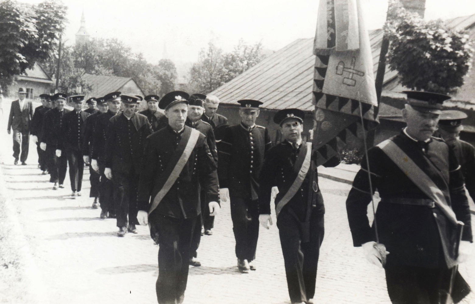 Slavnostní průvod. Vpravo dům čp. 373 (Zahradnictví Antonín Dvořák), vlevo vzadu dům čp. 366 a na pozadí věž kostela sv. Petra z Alkantary (S laskavým svolením p. Karla Pastuszka, ze soukromé sbírky)