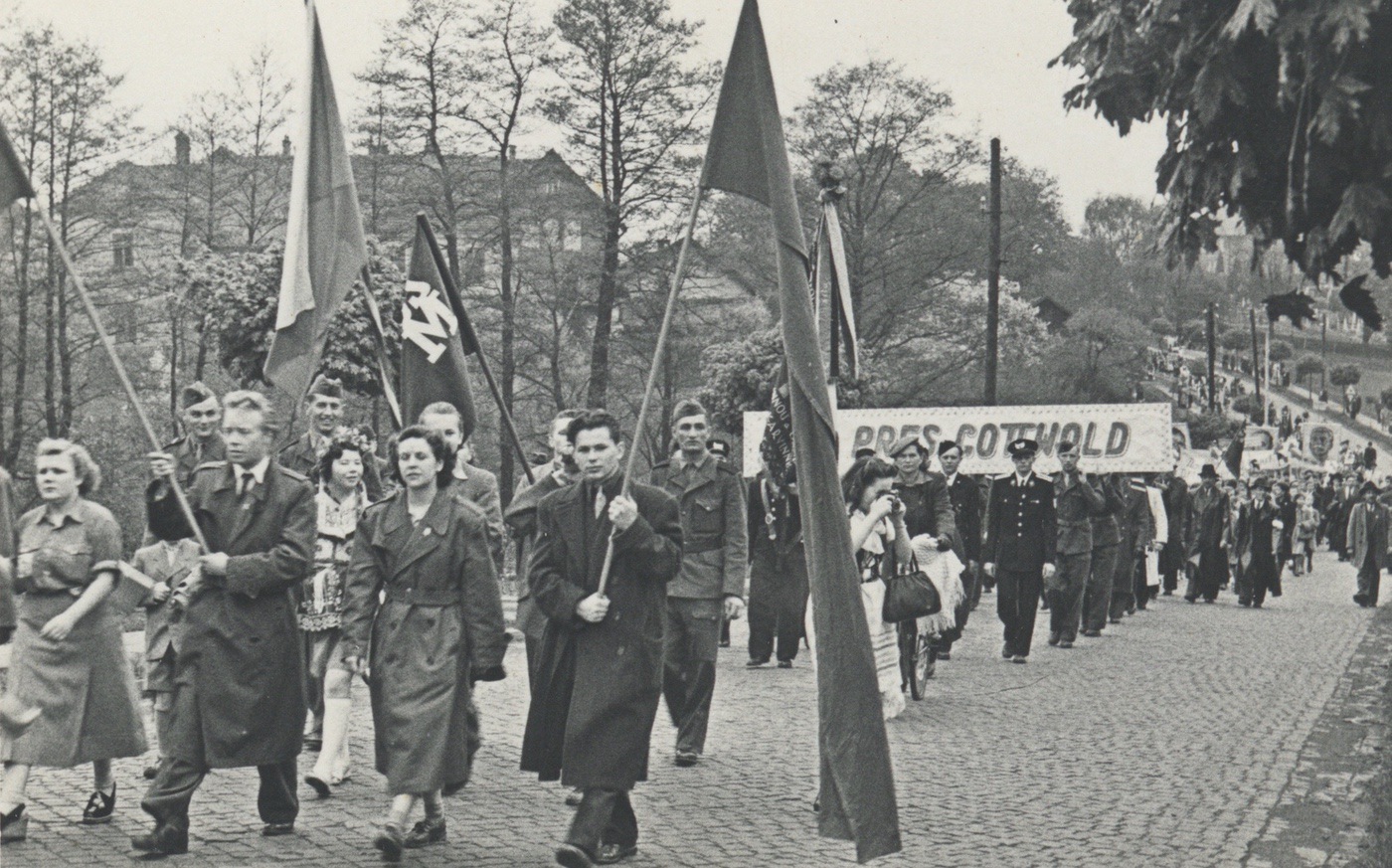 Prvomájový průvod procházející Komenského ulicí v roce 1951. V pozadí budova tzv. Červené školy (čp. 645).