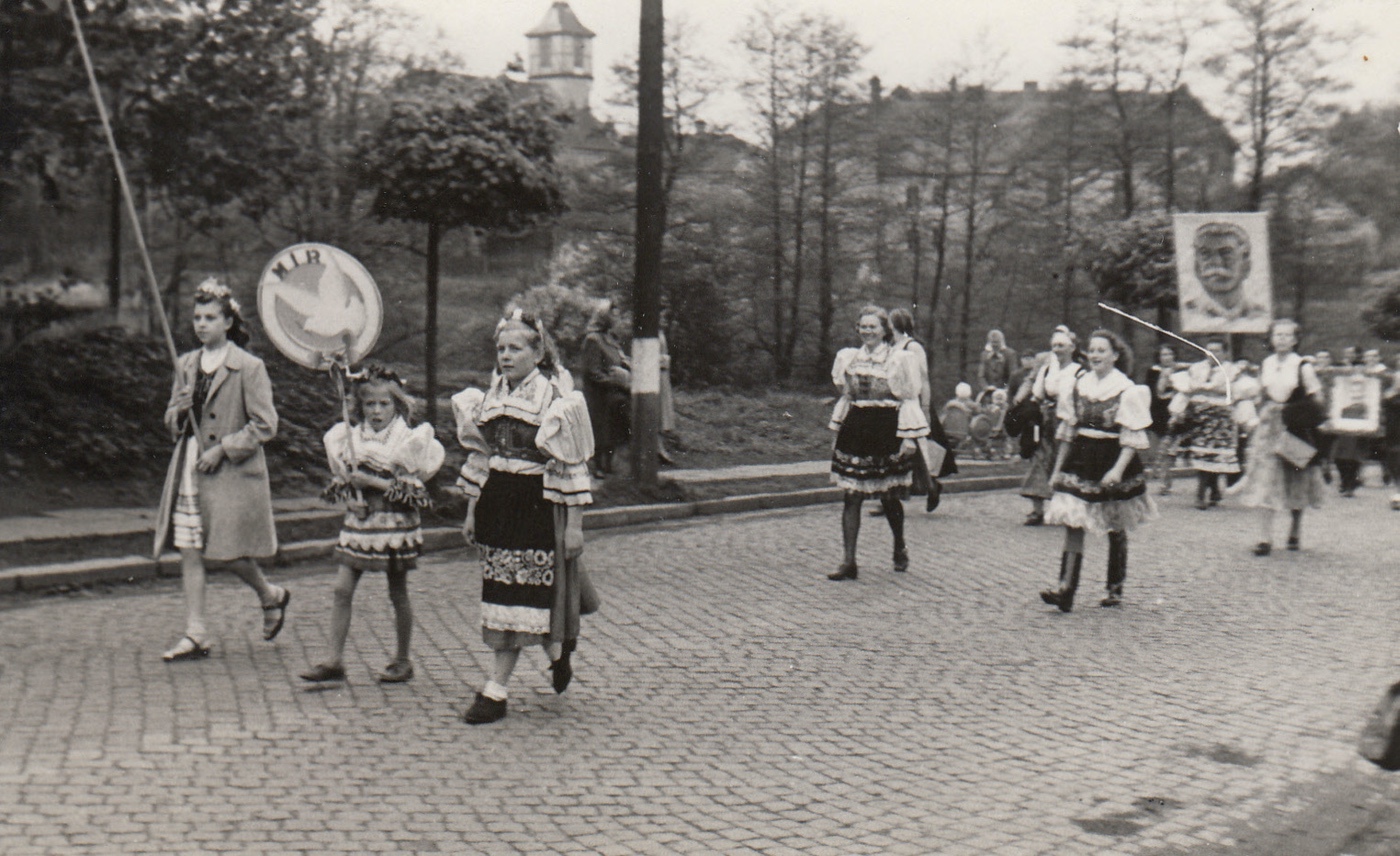 Prvomájový průvod procházející Komenského ulicí v roce 1951. V pozadí zleva kostel sv. Petra z Alkantary a budova tzv. Červené školy (čp. 645).