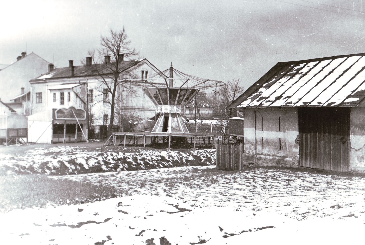 Záběr z místa kolejí MDOK a Báňské dráhy směrem k Závodnímu hotelu. Za kolotočem a střelnicí je Četnická stanice čp. 692. Vpravo je částečně vidět dům čp. 337 a vlevo kousíček domu čp. 789. Vzadu pak průčelí domu čp. 787. Před kolotočem je patrné koryto Karvinského potoka a v pravé části snímku je stodola náležející k domu čp. 60. Varianta s vyznačenými čísly popisnými na následujícím snímku… (Identifikace a označení objektů: Petr Bindač)