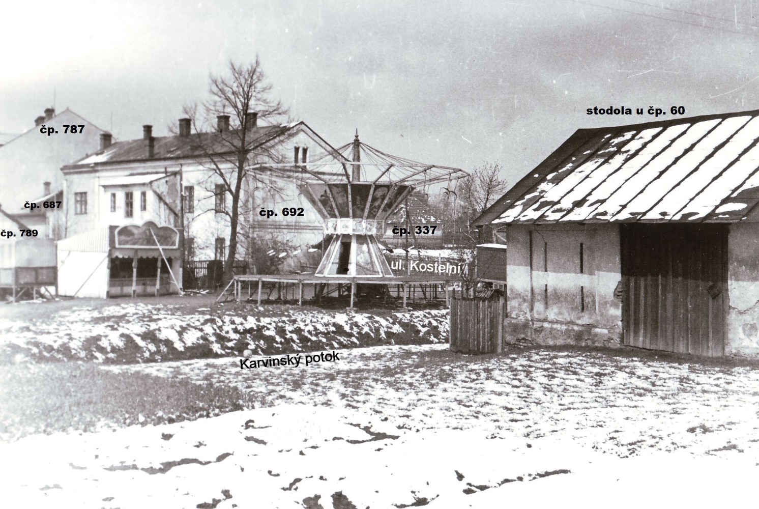 Záběr z místa kolejí MDOK a Báňské dráhy směrem k Závodnímu hotelu. Za kolotočem a střelnicí je Četnická stanice čp. 692. Vpravo je částečně vidět dům čp. 337 a vlevo kousíček domu čp. 789. Vzadu pak průčelí domu čp. 787. Před kolotočem je patrné koryto Karvinského potoka a v pravé části snímku je stodola náležející k domu čp. 60. (Identifikace a označení objektů: Petr Bindač)
