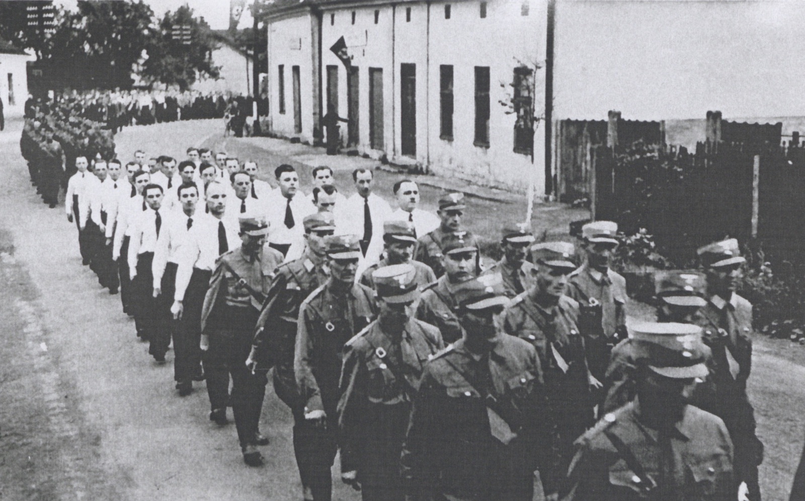 Slavnostní vojenský průvod v době německé okupace na Komenského ulici. V pozadí vpravo dům čp. 84 (Řeznictví Folwarczny), úplně vlevo část domu čp. 15 a v zatáčce vzadu průčelí domu čp. 582.