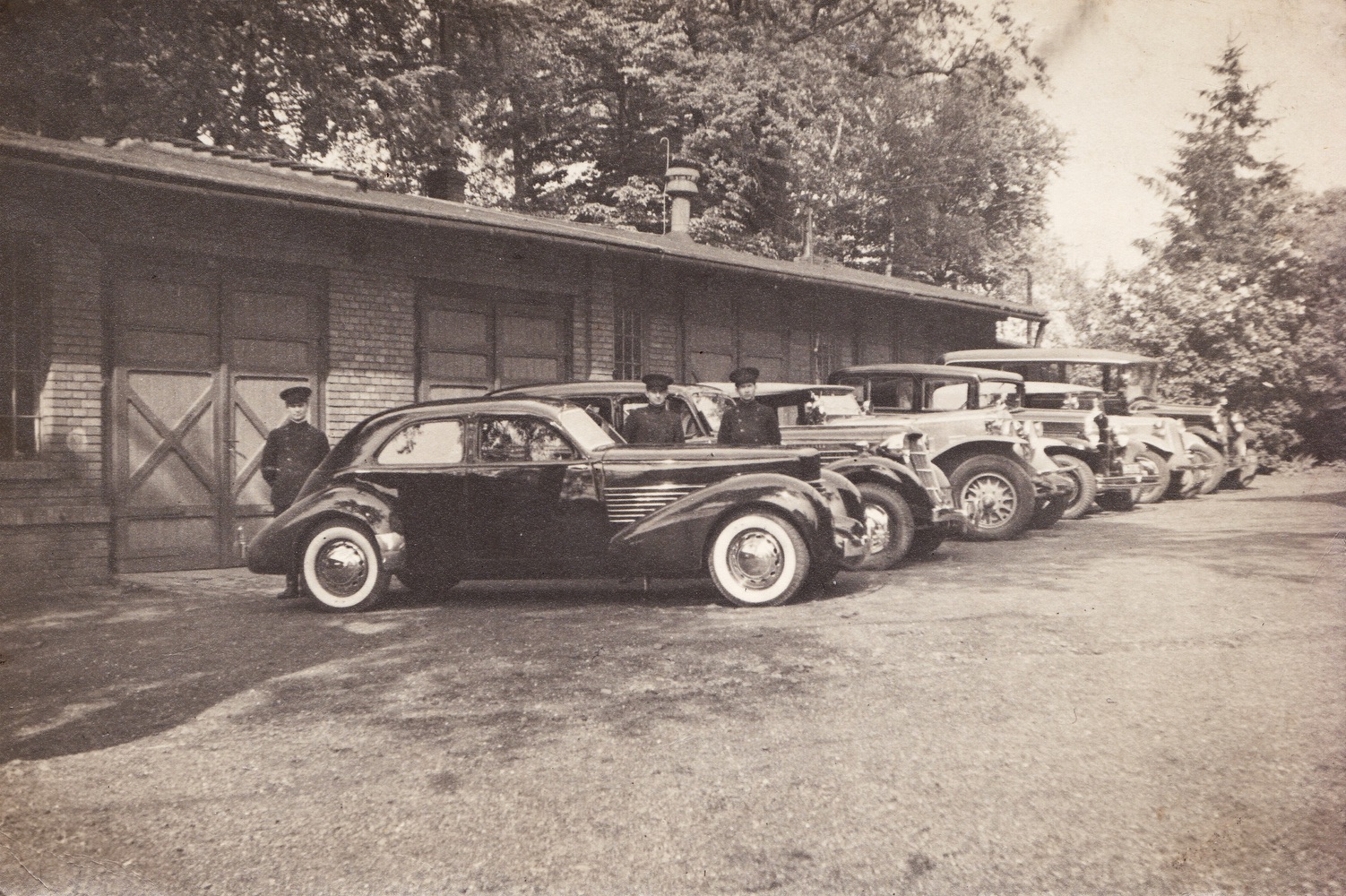 Budova starých garáží v popředí s automobilem Cord 810. Muži na fotografii zleva: hlavní řidič Eduard Horek a řidičové Alois Owczarzy a Karl Walek. Fotografie vznikla mezi květnem a říjnem roku 1936 (Zdroj: E. Schweserová, P. Bindač: SOLCA Tajemství zámeckého parku = KLIK NA FOTOGRAFII. Foto z rodinné sbírky Heleny Lukoszové)