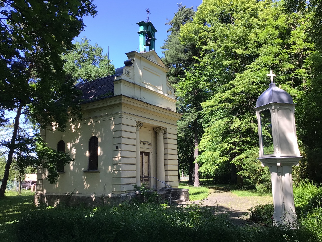Panna Maria s Jezulátkem v prosklené schráně zdobeného, dřevěného sloupu a v pozadí kaple sv. Anny (Darkov)