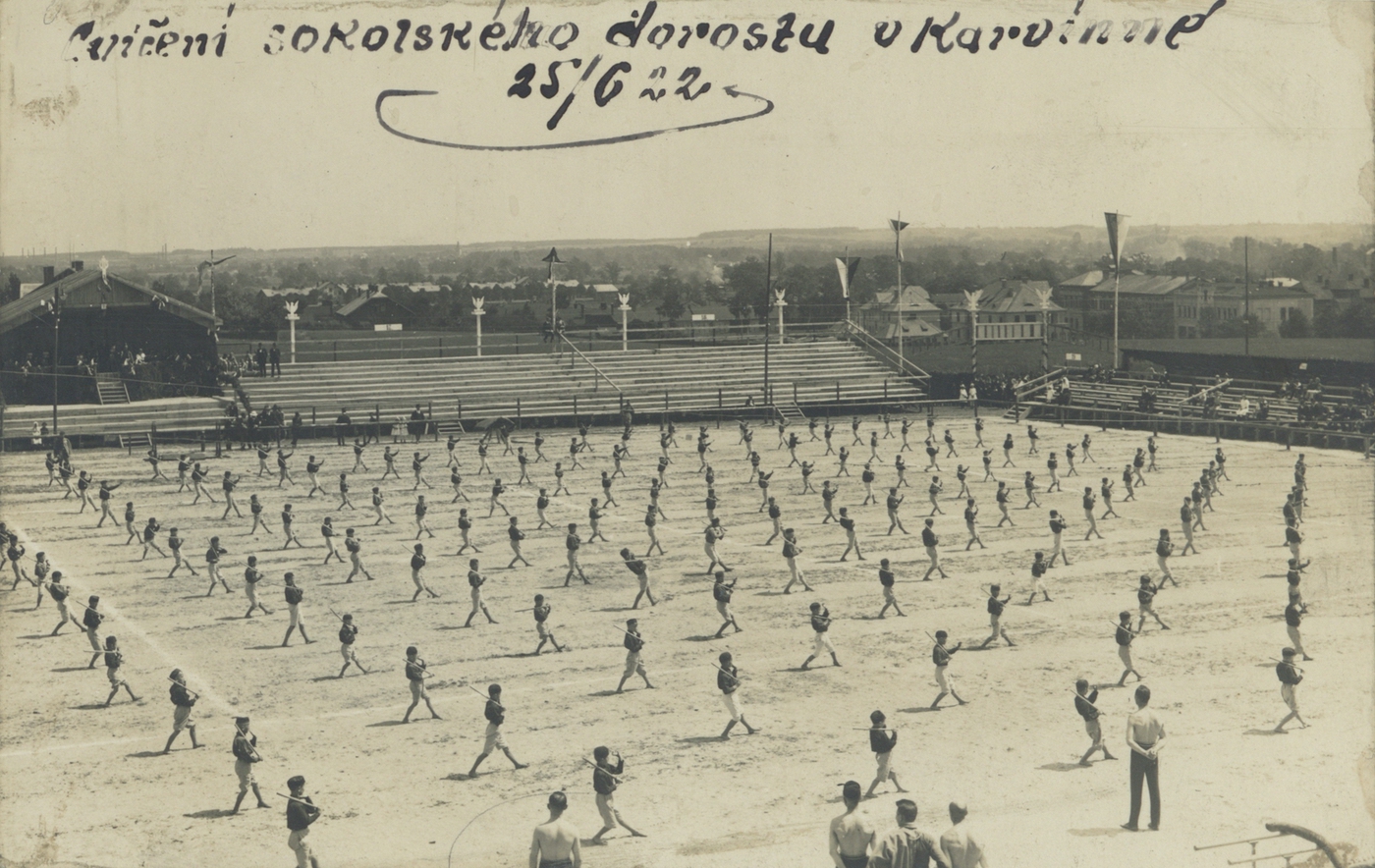 Cvičení sokolského dorostu na hřišti německého klubu Deutscher Sportverein Karwin 25.6.1922. Vpravo v pozadí budova Závodního hotelu a obchodního domu M. Glesinger.