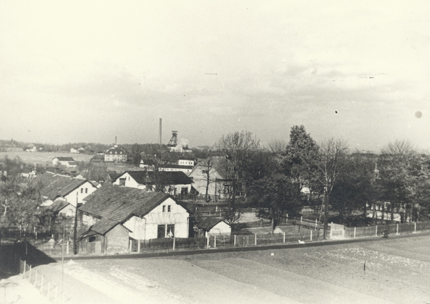 V popředí domy z Rajkovy kolonie čp. 189 a čp. 190. Za nimi přízemní domek čp. 869 (řeznictví Folwarczny), napravo od něj větší dům: potraviny Bielesz čp. 404. Vpravo je mezi stromy vidět věžička kaple (márnice). Vzadu na obzoru důl Františka a patrový dům se třemi vikýři: učitelský dům čp. 1371 (Fotografováno z domu čp. 1658). 