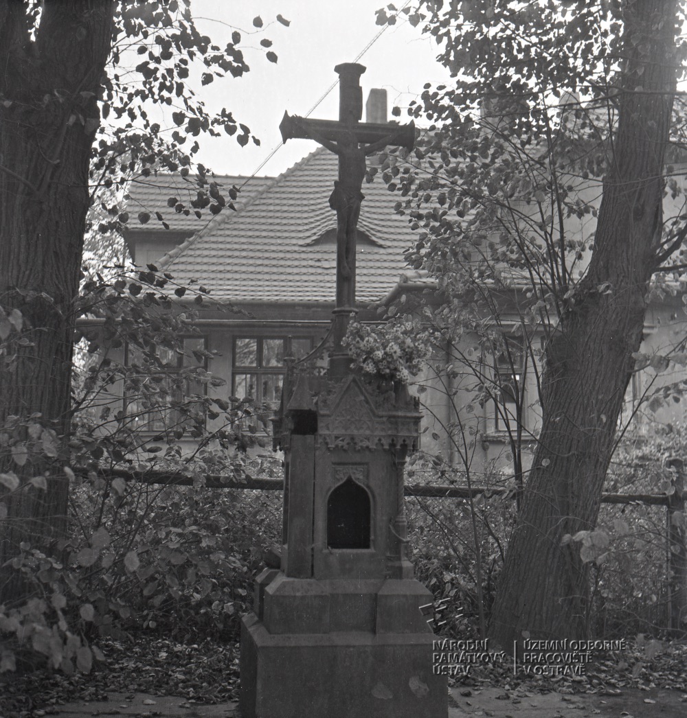 V popředí litinový kříž u Závodní nemocnice, v pozadí dům čp. 1401: vila primáře MUDr. Bayera (Zdroj: Národní památkový ústav, územní odborné pracoviště v Ostravě. Autor fotografie: Svátková. Datum pořízení: září 1965. Číslo snímku: A 7950)