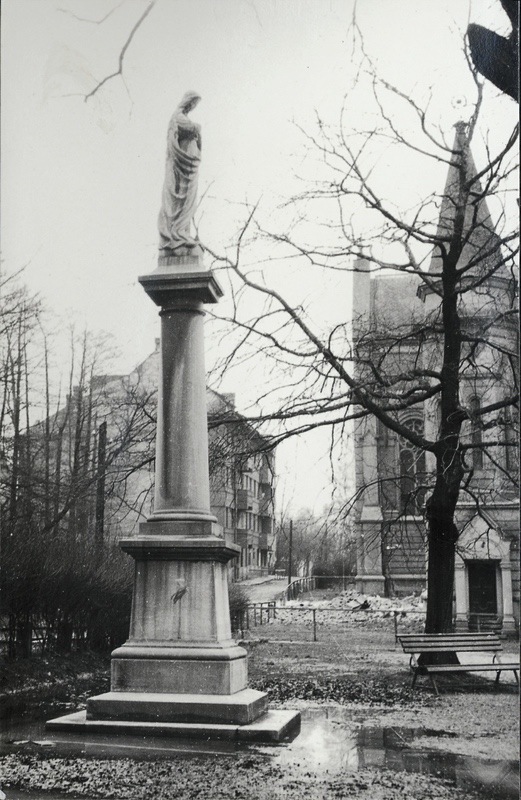 Kamenný sloup se sochou Panny Marie před kostelem sv. Jindřicha, v pozadí obytný dům čp. 1558