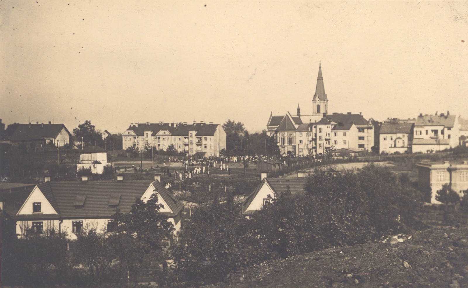 Hasiči při cvičení na sokolském cvičišti v centru staré Karvinné. Fotografováno z haldy u dolu Gabriela. V popředí zleva doprava (Lelkova ulice): dům čp. 1456, zpola zakrytý dům čp. 1457 a část vily čp. 1570 (Stavitel Daniel). V pozadí zleva doprava: dům čp. 61, obytné domy čp. 1440 a 1441, dům čp. 1655, 1625 a 1656. Vzadu kostel sv. Jindřicha.